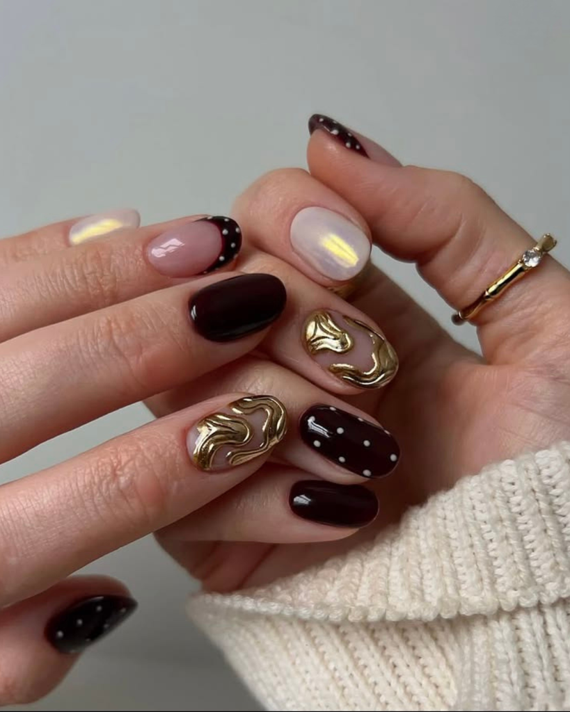 Short dark cherry nails with gold chrome swirls, white polka dots and a pearl accent. Short nail design